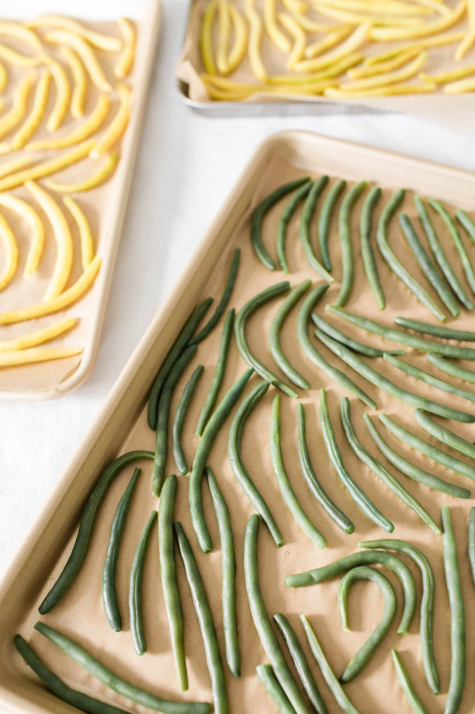 Two baking sheets lined with parchment paper, one containing neatly arranged green beans and the other yellow beans, prepared for freezing.