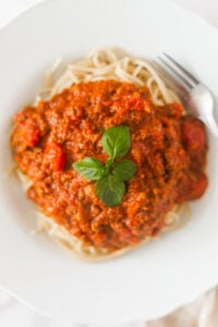 A plate of spaghetti topped with a generous serving of meat and tomato sauce, garnished with fresh basil leaves, with a fork placed on the side.