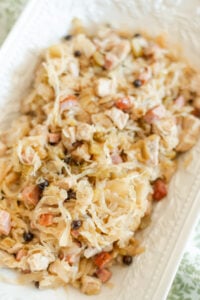 A close-up of a dish featuring chopped meat, sauerkraut, and vegetables mixed together, served on a white rectangular plate. The ingredients appear tender and well-blended, with visible bits of sausage and herbs.
