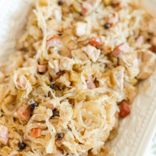 A close-up of a dish featuring chopped meat, sauerkraut, and vegetables mixed together, served on a white rectangular plate. The ingredients appear tender and well-blended, with visible bits of sausage and herbs.