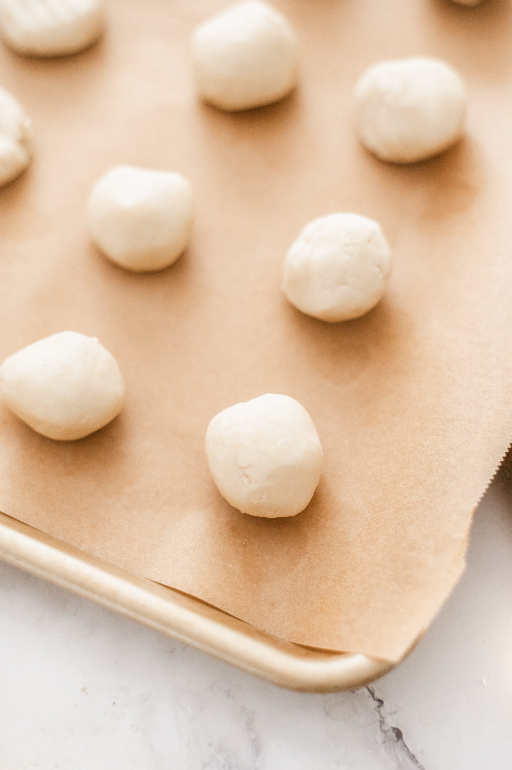 Balls of Traditional Shortbread Cookie dough are arranged in rows on a baking sheet lined with brown parchment paper, ready to be baked.