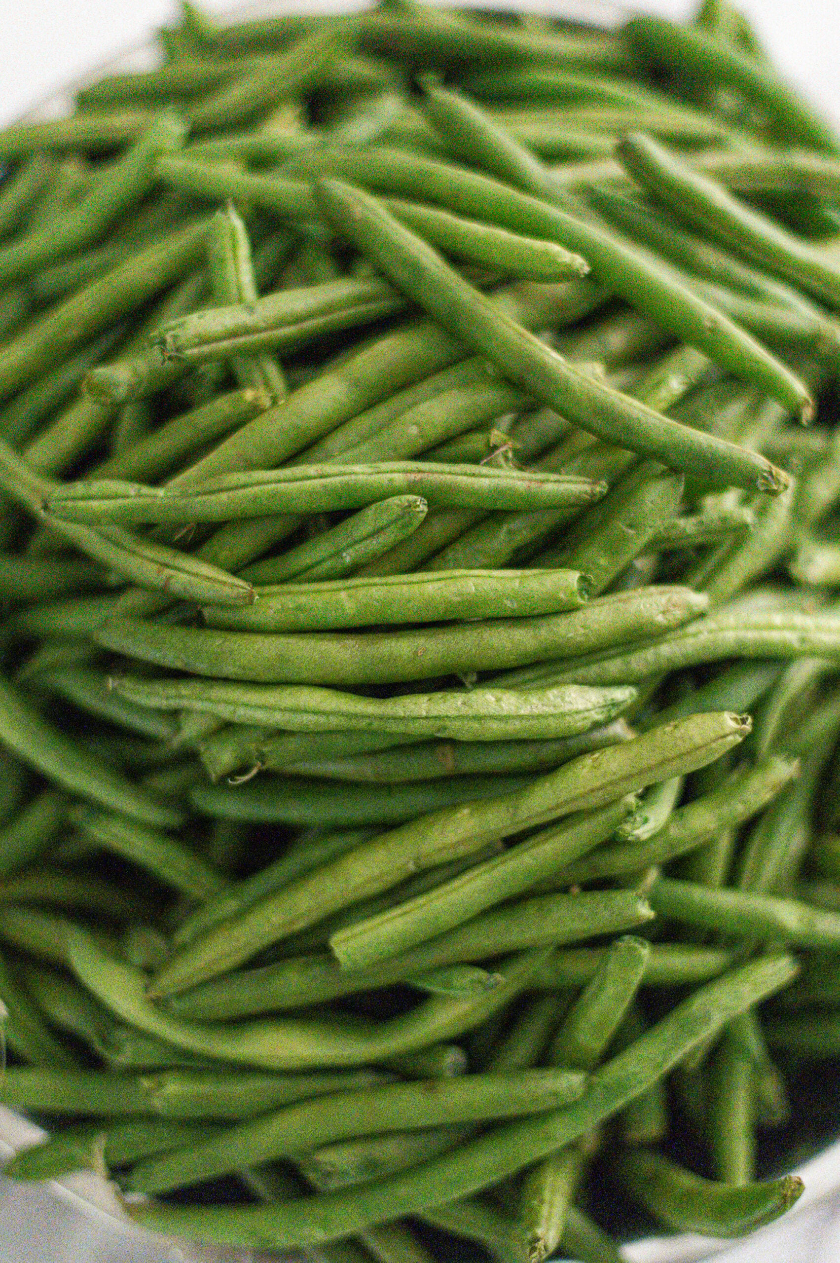 A pile of fresh green beans, closely stacked together, shows their smooth, elongated shape and vibrant green color—perfect for learning how to can green beans in a pressure canner.