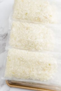 Three vacuum-sealed bags filled with chopped onions are stacked on a tray with a white marble background.
