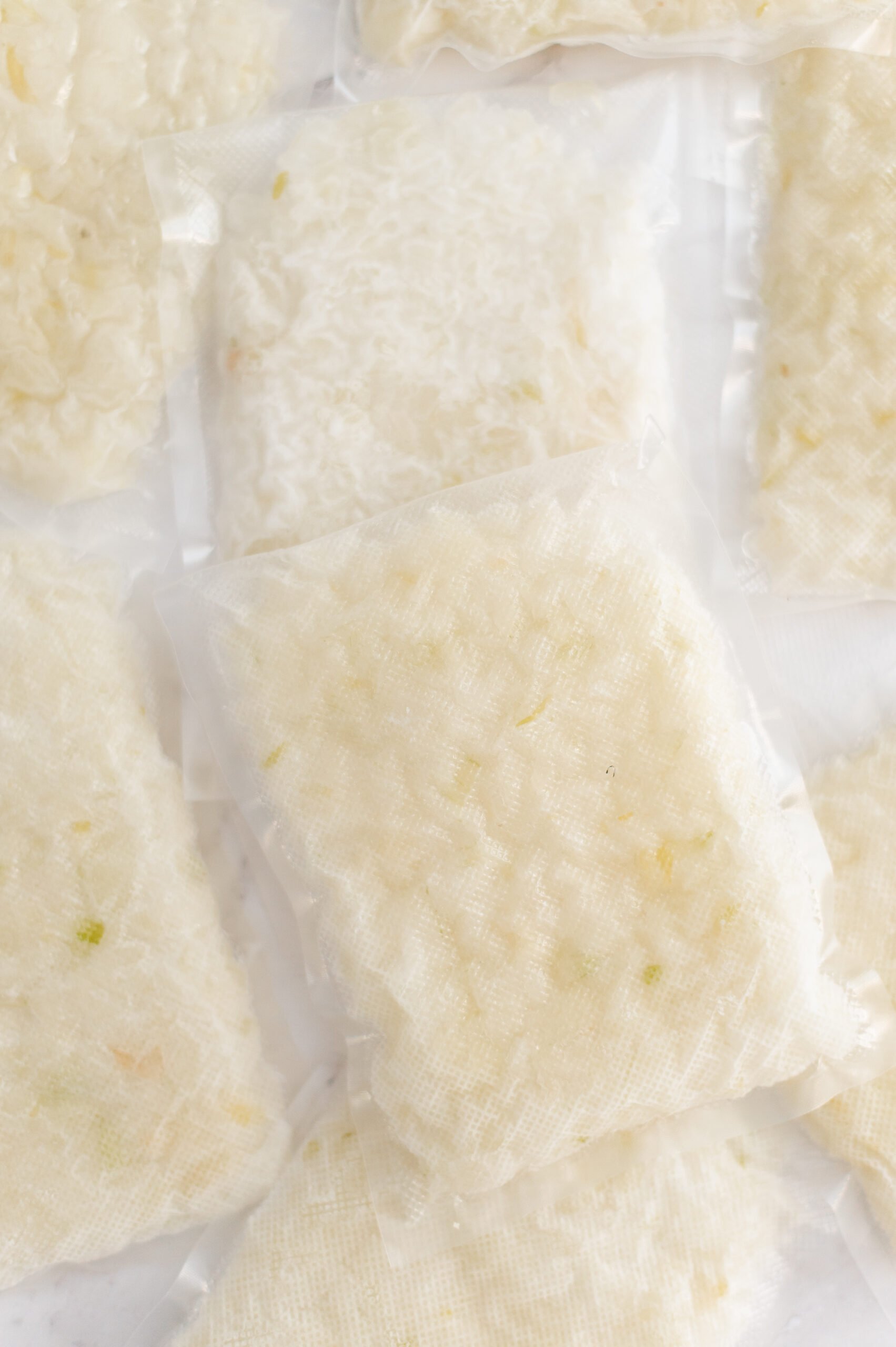 Several vacuum-sealed plastic packets filled with cooked white rice are arranged on a white surface. The rice is visible through the transparent packaging.