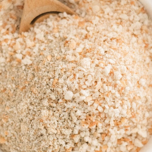 A close-up of a bowl filled with light-colored, coarse breadcrumbs being stirred with a wooden spoon—perfect for illustrating How to Make Homemade Breadcrumbs.