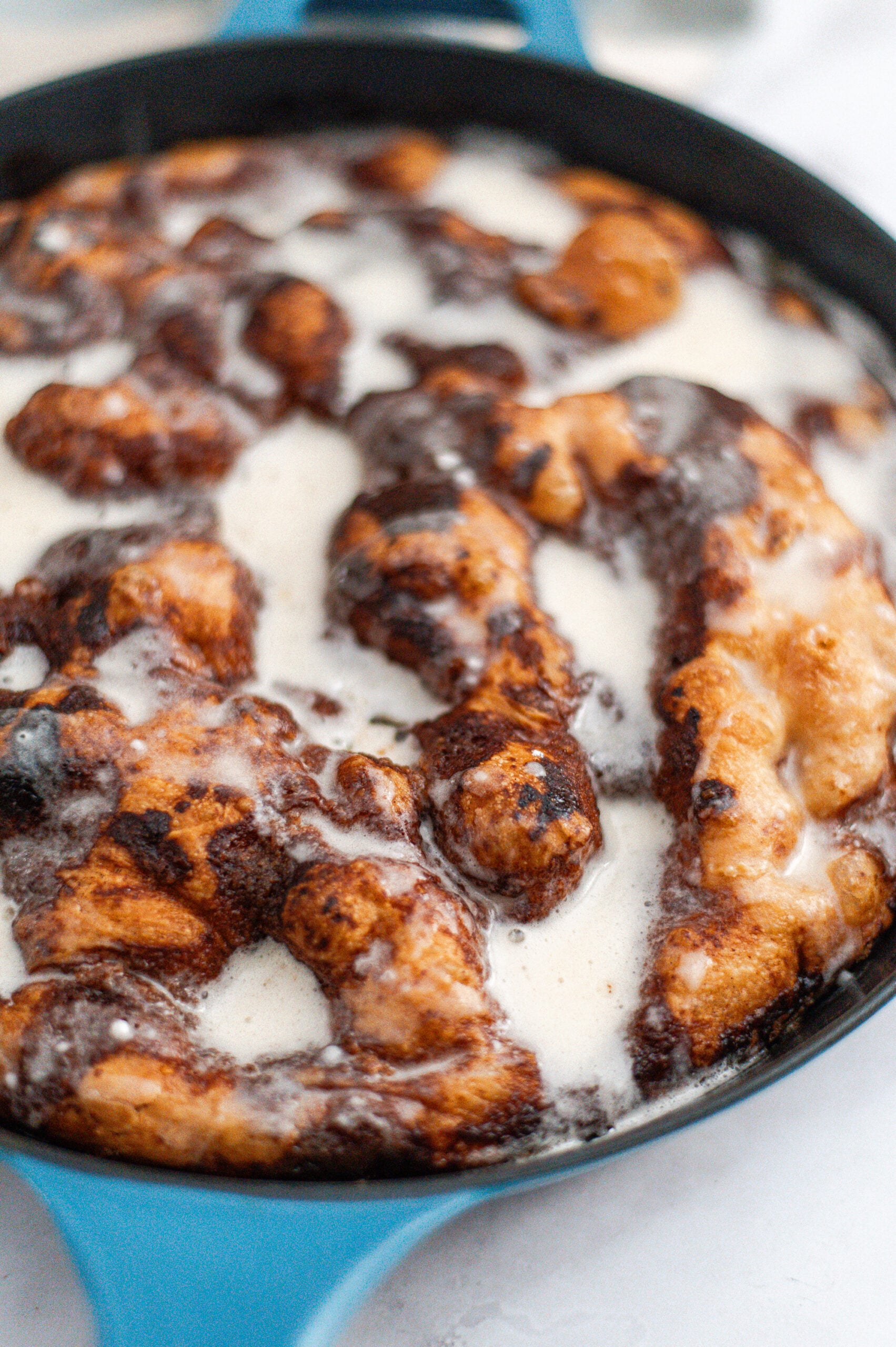 A close-up of freshly baked cinnamon rolls in a blue pan, topped with melting white icing and swirls of cinnamon.