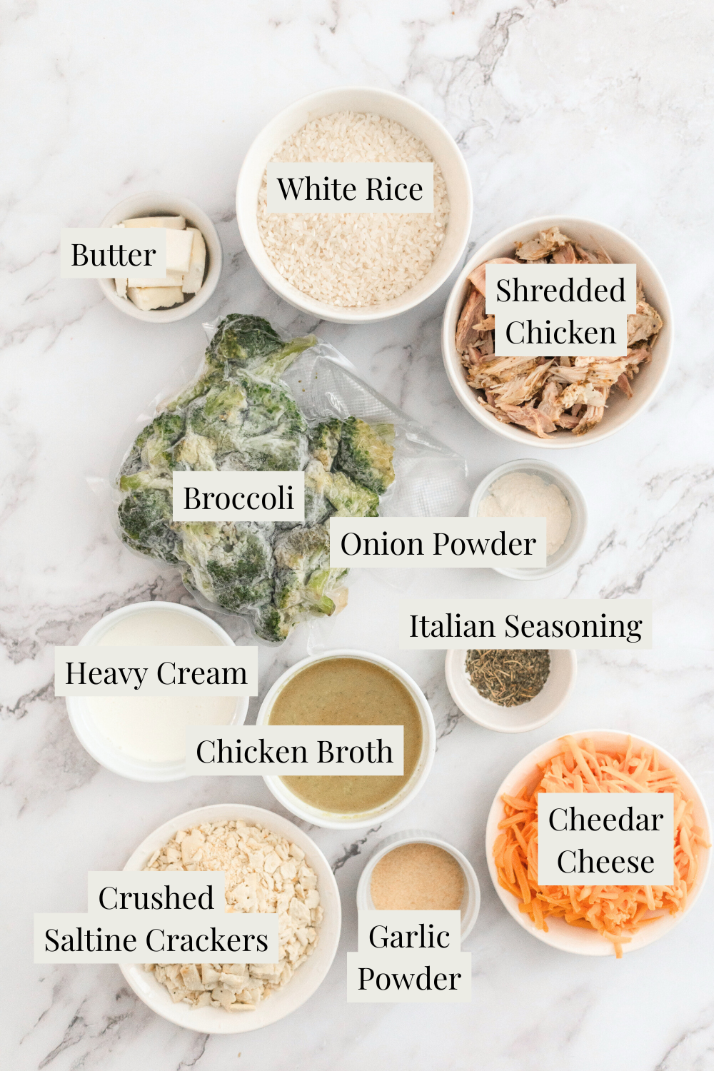 A top-down view of ingredients for Broccoli Chicken and Rice Casserole: bowls of white rice, shredded chicken, broccoli, butter, heavy cream, chicken broth, onion powder, Italian seasoning, crushed saltine crackers, garlic powder, and cheddar cheese.
