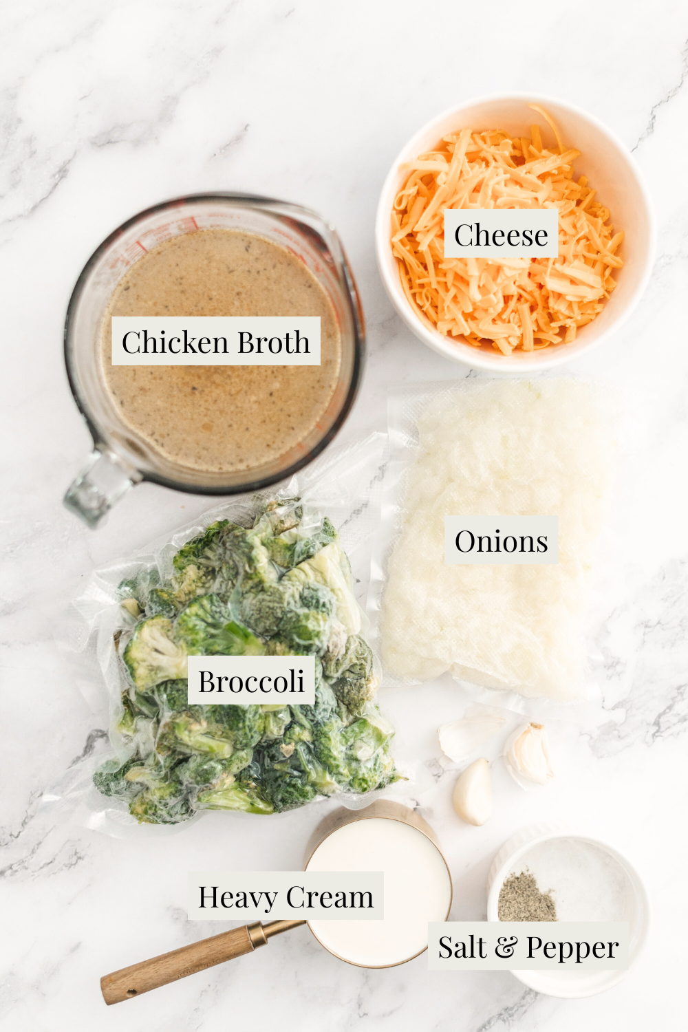 A flat lay of labeled ingredients for Cream of Broccoli Soup on a white surface: cheese, chicken broth in a measuring cup, a bag of onions, frozen broccoli, heavy cream, garlic clove, and small bowls of salt and pepper.