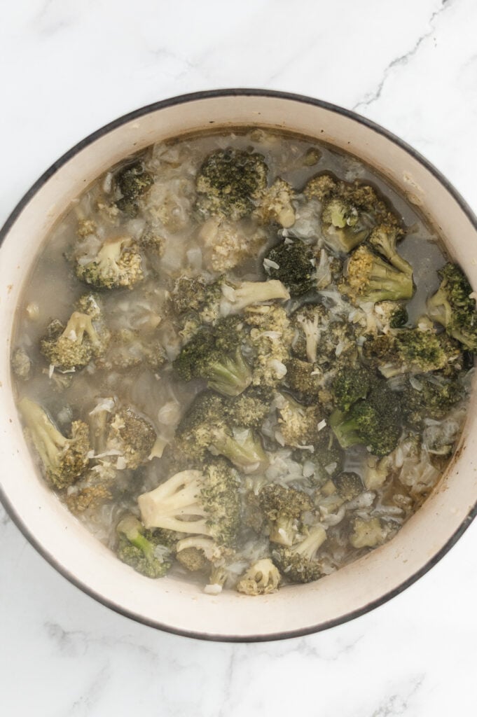 A pot filled with cooked broccoli florets in a light, watery broth—perfect for transforming into a delicious Cream of Broccoli Soup—sits on a white marble surface.