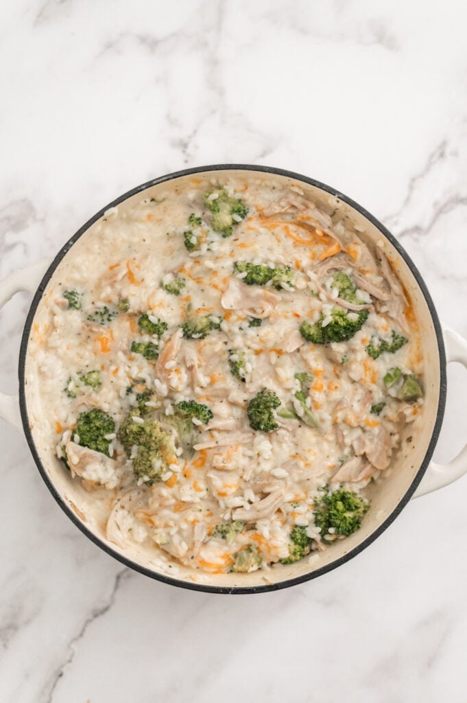 A creamy Broccoli Chicken and Rice Casserole with shredded chicken, broccoli florets, and melted cheese in a round white pot, viewed from above on a marble countertop.